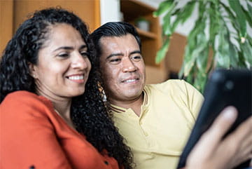 woman and man sitting on sofa reading tablet device